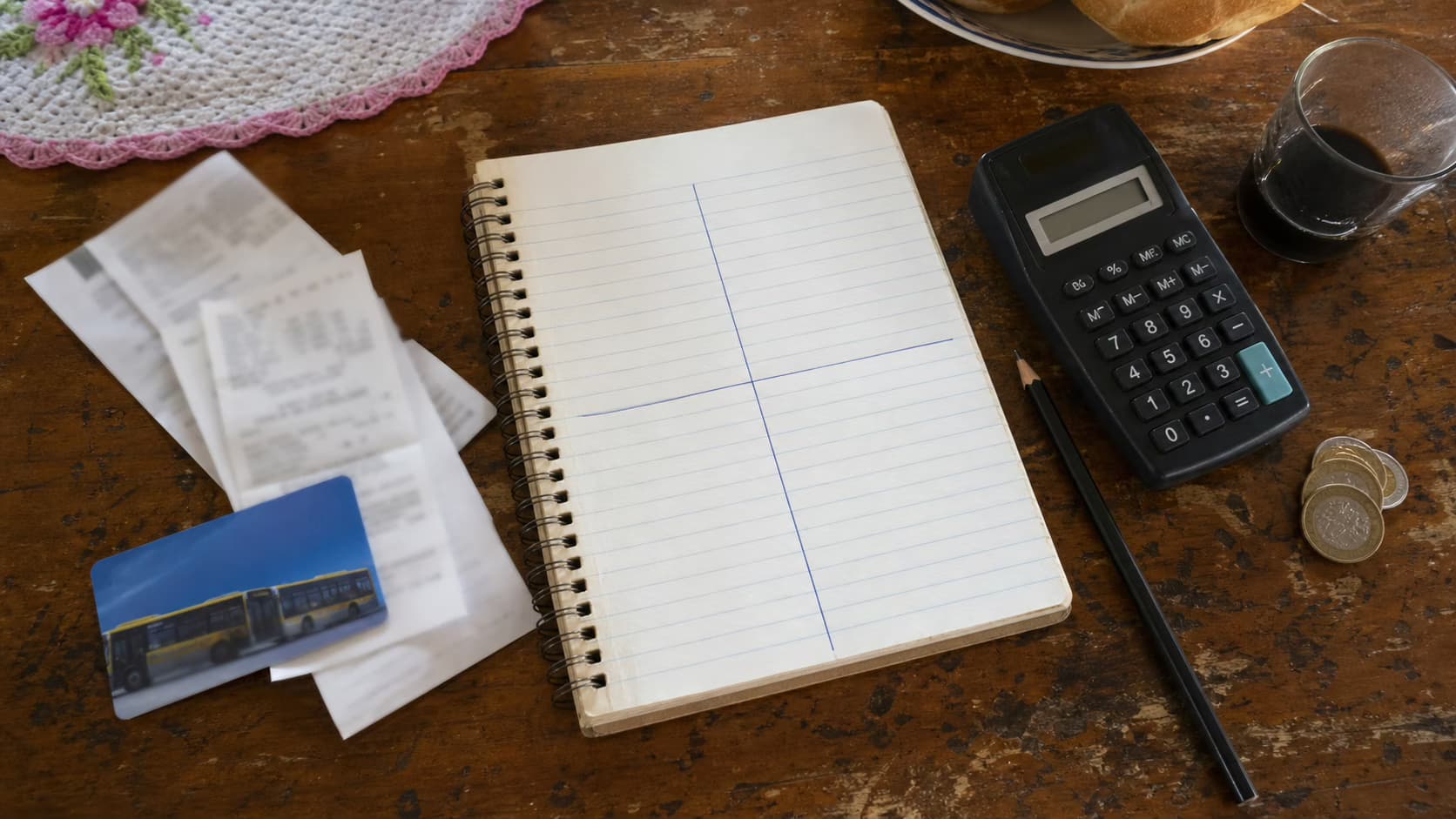 Caderno dividido em quatro blocos ao lado de contas, recibo de mercado e calendário para organizar um orçamento com pouca margem.
